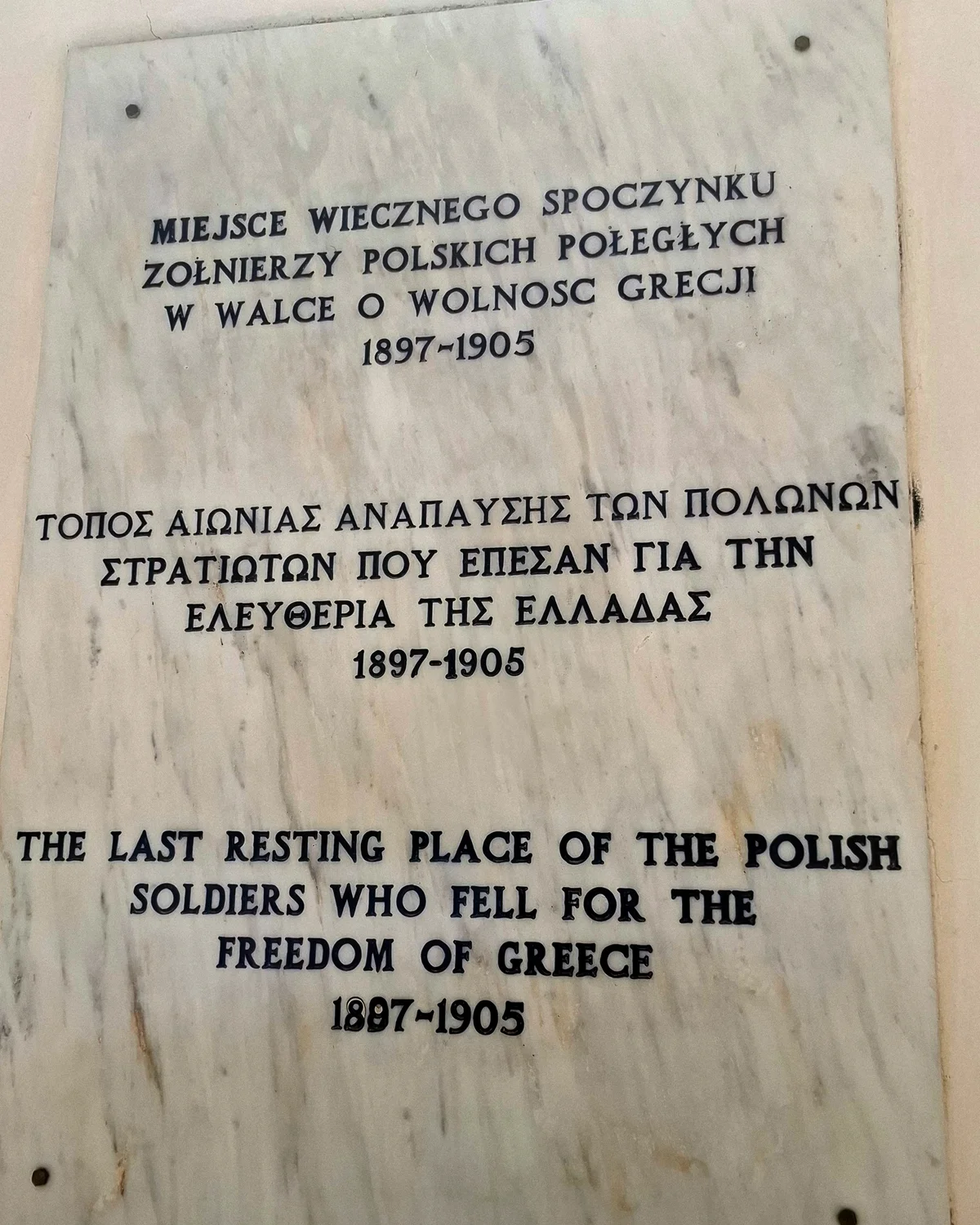 Tablica na murze polskiego cmentarza w Rethymno z napisem w języku polskim, greckim i angielskim